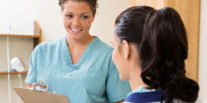 Smiling health worker with clipboard talking to patient